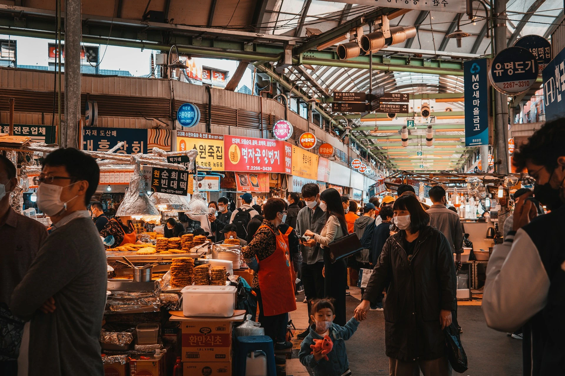 Bustling traditional Korean food market with vendors cooking various dishes, steam rising from cooking pots, customers seated